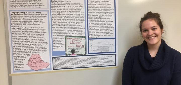 Carly Marten smiling and standing next to a poster of her undergraduate thesis