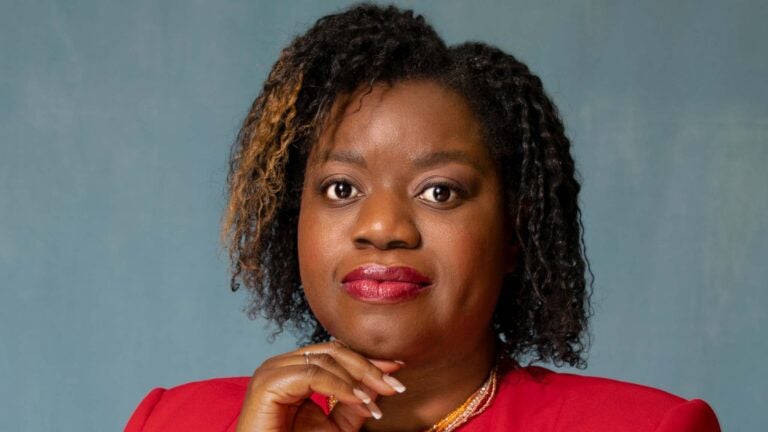 Guerline Jozef with wearing a red blazer and white top stands in front of a plain blue background.