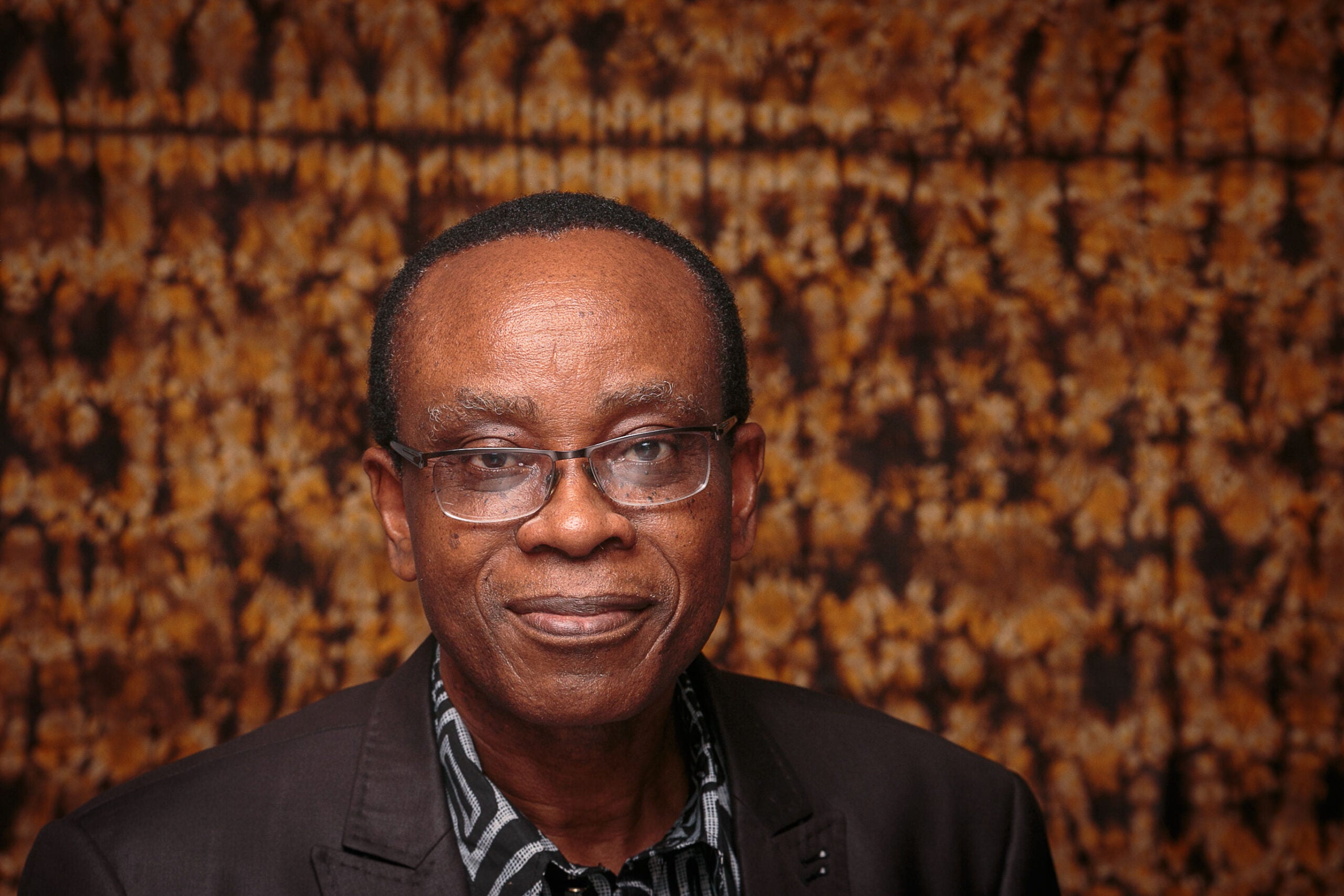 This photograph shows a Nnimmo Bassey in front of an orange patterned background.
